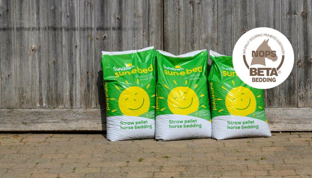 Three bags of Sundown Sun-e-bed bedding in front of a wooden barn door, with a graphic of the BETA NOPS logo