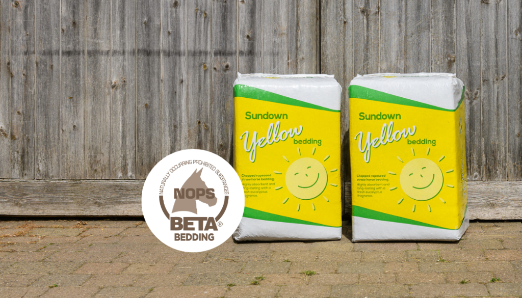two bales of Sundown Yellow bedding in front of a wooden barn door, with a graphic of the BETA NOPS logo