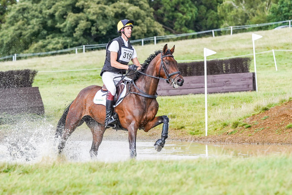 Will Rawlin riding a bay horse through water on a cross country course