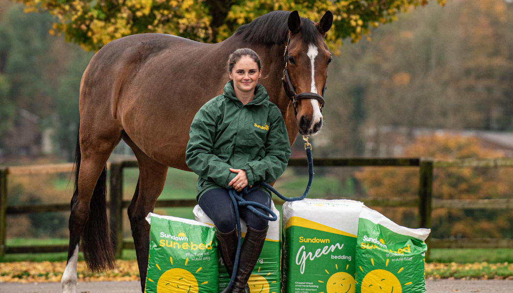 Woman sits on bales of Sundown bedding with a horse behind her