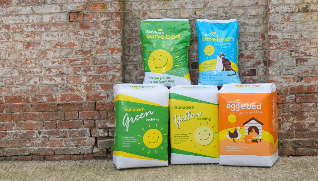 Brightly coloured bales of Sundown equine bedding, chicken bedding and cat litter stacked in front of a wooden barn door